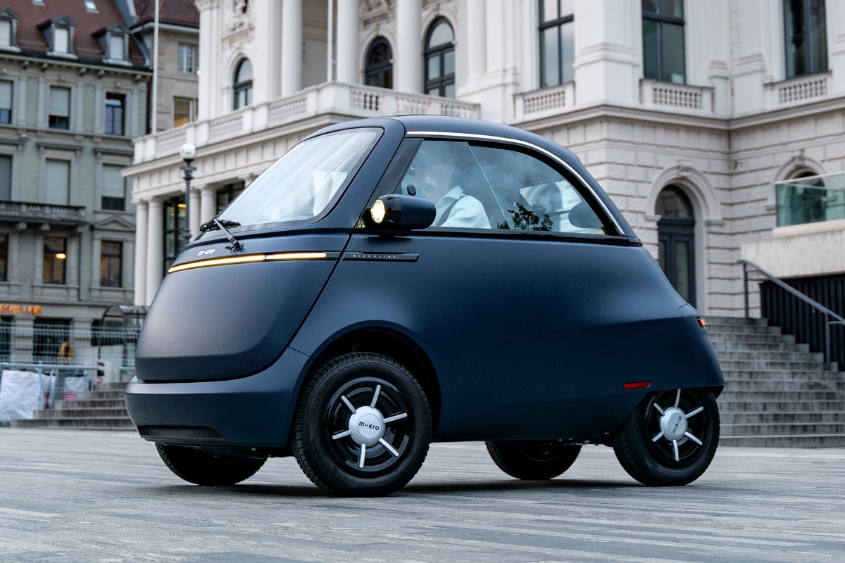 Blue Microlino parked beside a stone building