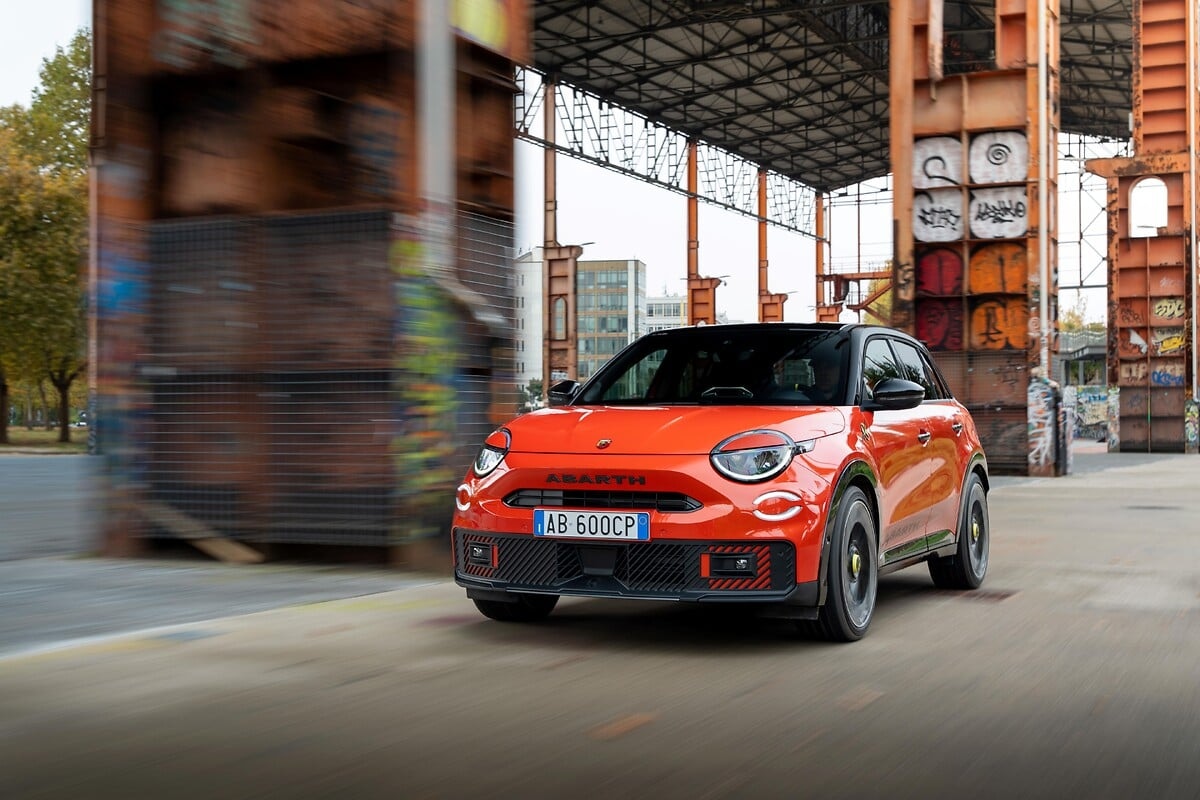 Orange Abarth 600e Competizione driving past an industrial building