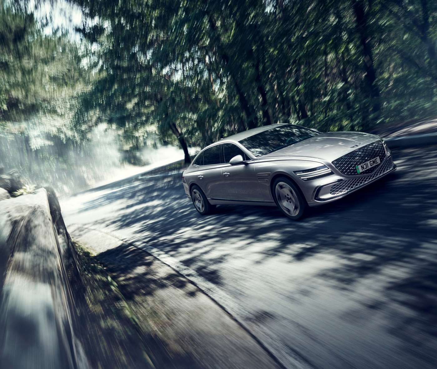 Silver updated Genesis Electrified G80 driving through woodland